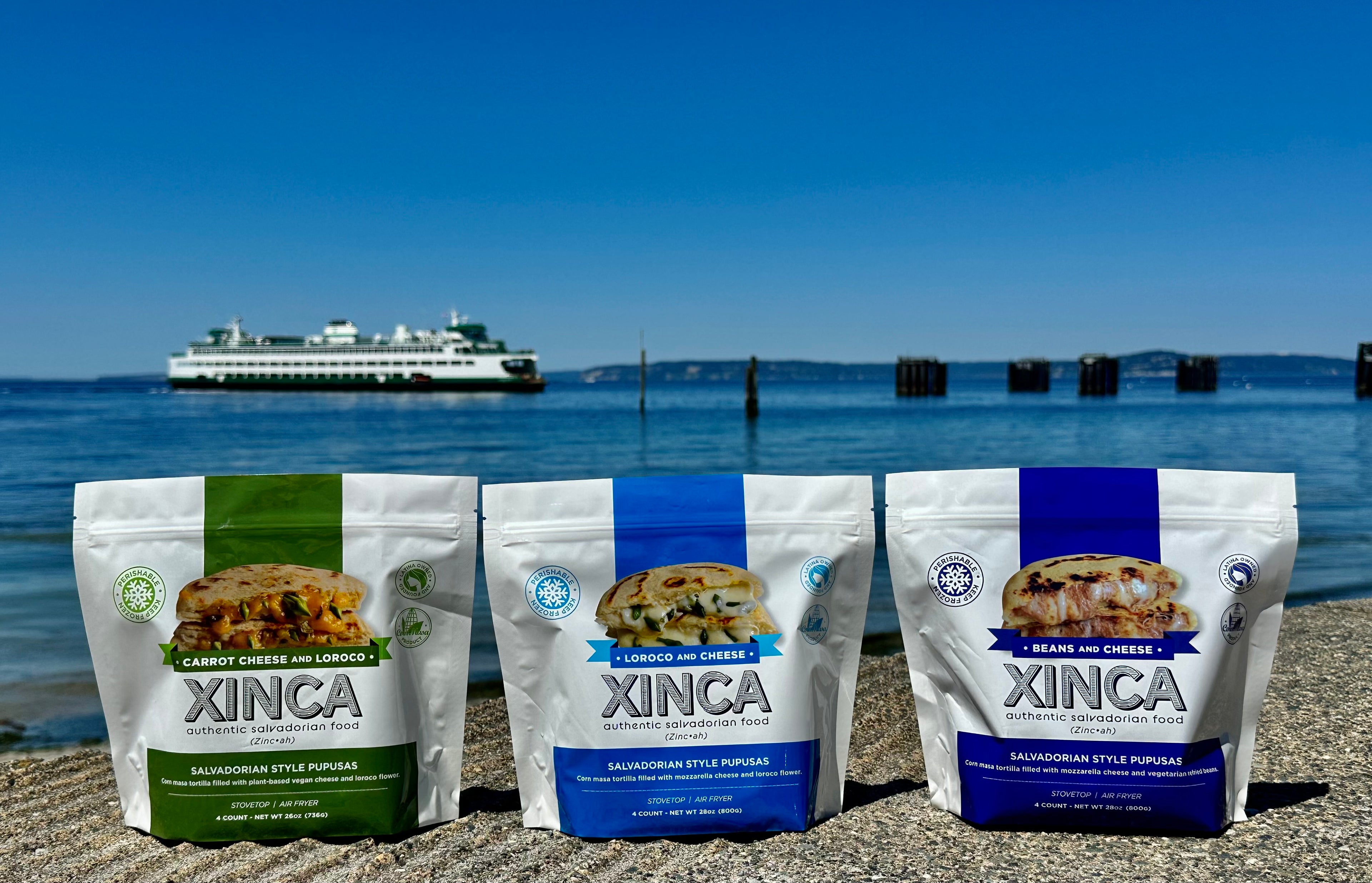 Carrot Cheese & Loroco, Loroco & Cheese, Beans & Cheese Pupusas packaging on cement with a water and boat background